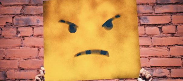 paper square angry face,held up in front of a brick wall