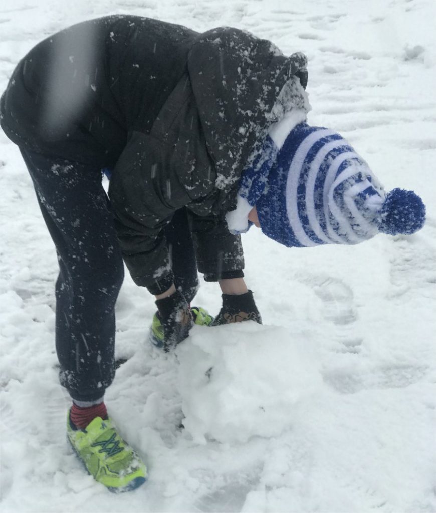 boy rolling a giant snowball to make a snowman base